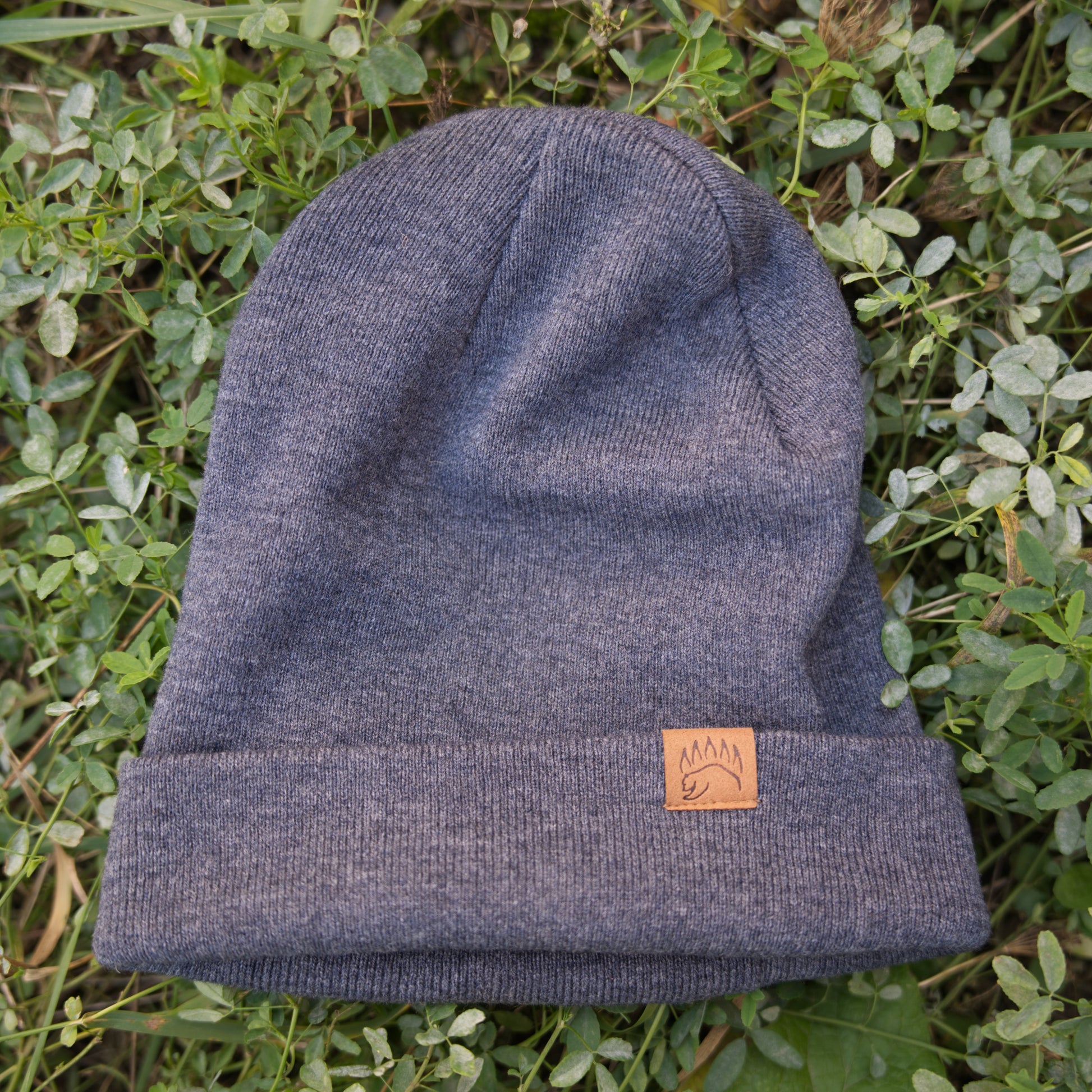 Charcoal 100% Soft Merino Wool Beanie with folded cuff and bear paw logo, displayed on grass for product showcase.