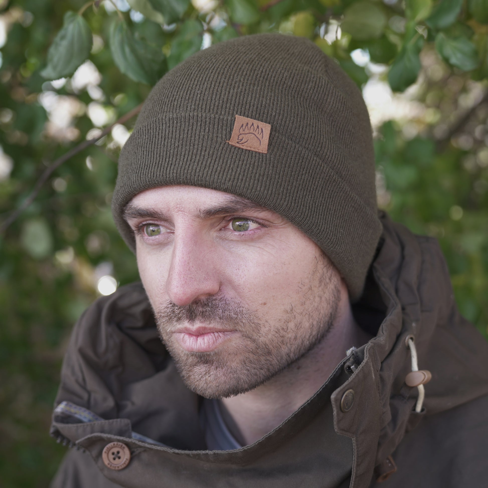 Olive green 100% Soft Merino Wool Beanie worn by man in brown jacket, featuring bear paw logo for a rugged outdoor look.