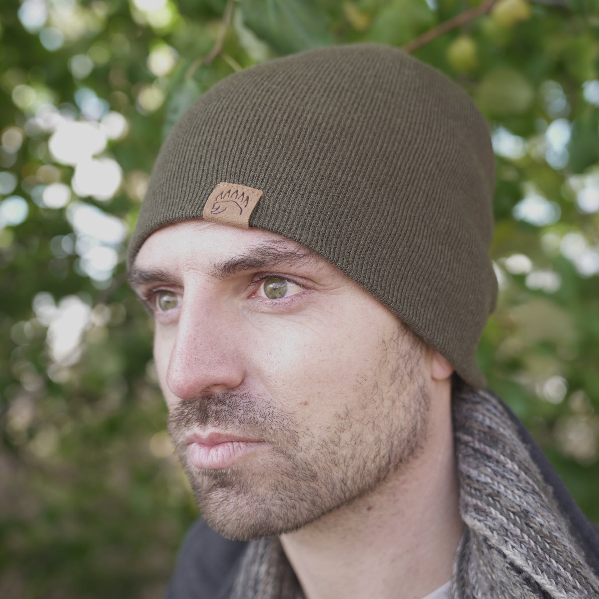 Close-up of man in olive 100% Soft Merino Wool Beanie with bear paw logo, ideal for cold weather and outdoor activities.