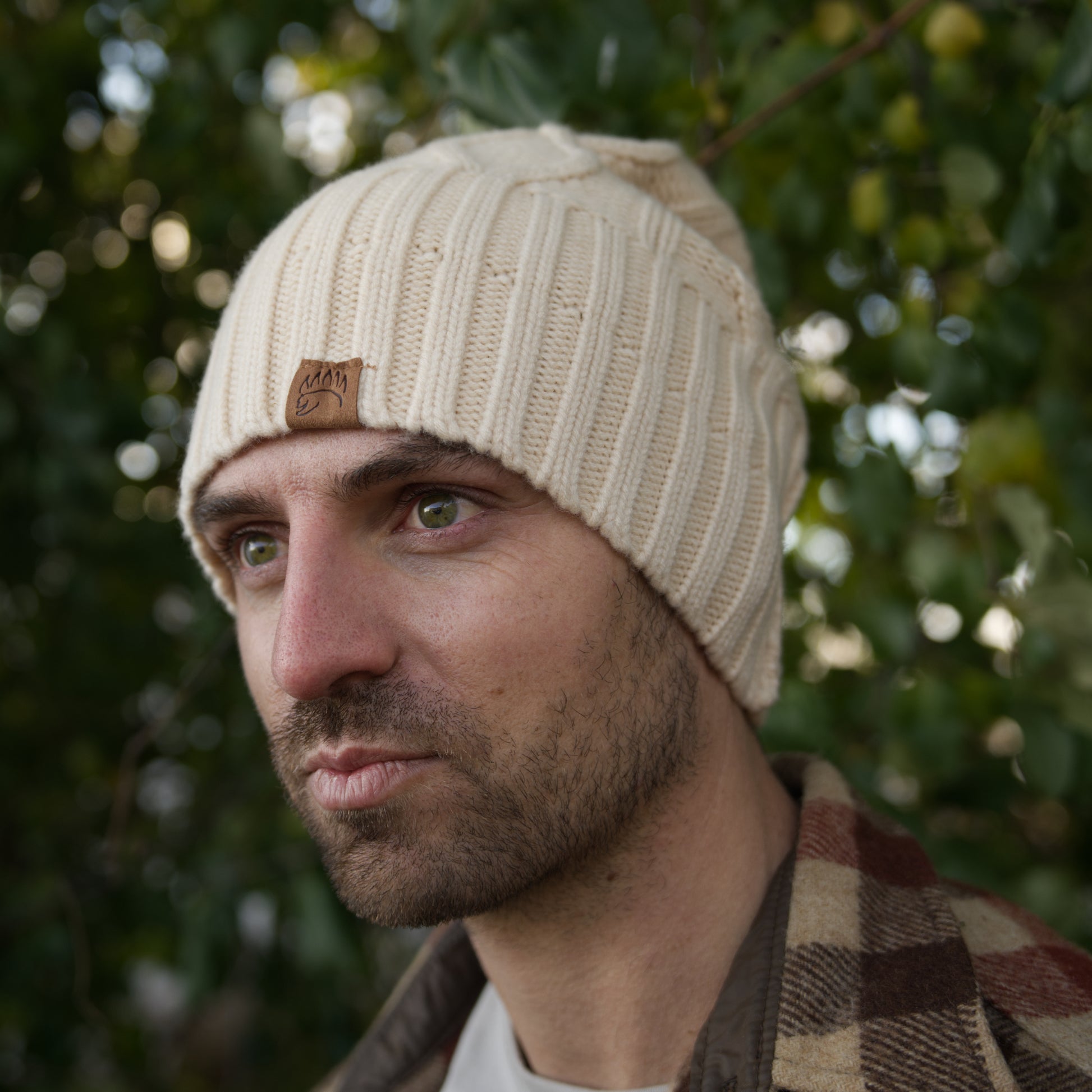 Cream cable-knit 100% Soft Merino Wool Beanie worn by man, showcasing thick ribbed cuff and leather bear paw patch.