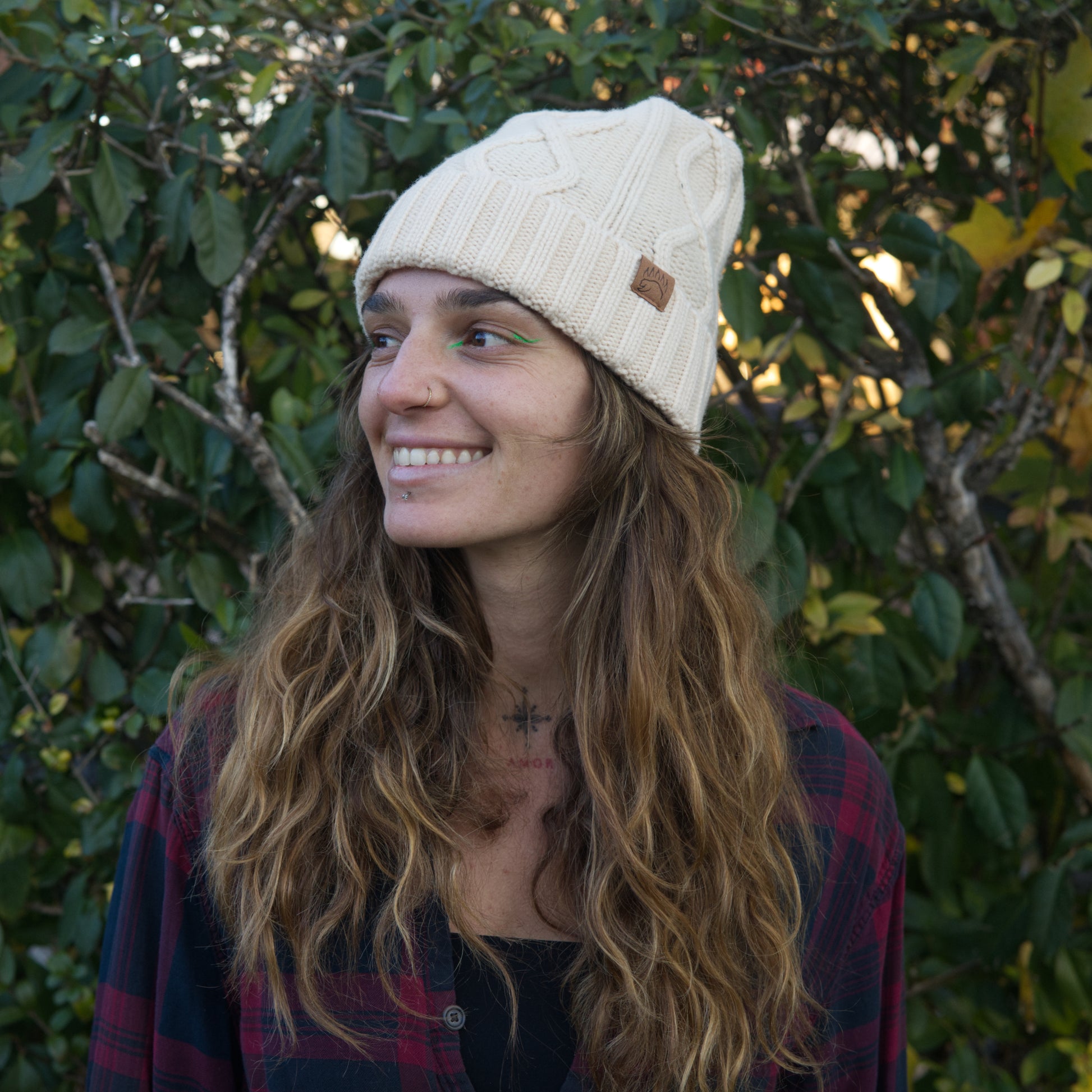Smiling woman wearing cream cable-knit 100% Soft Merino Wool Beanie with bear paw logo, cozy and stylish for winter fashion.