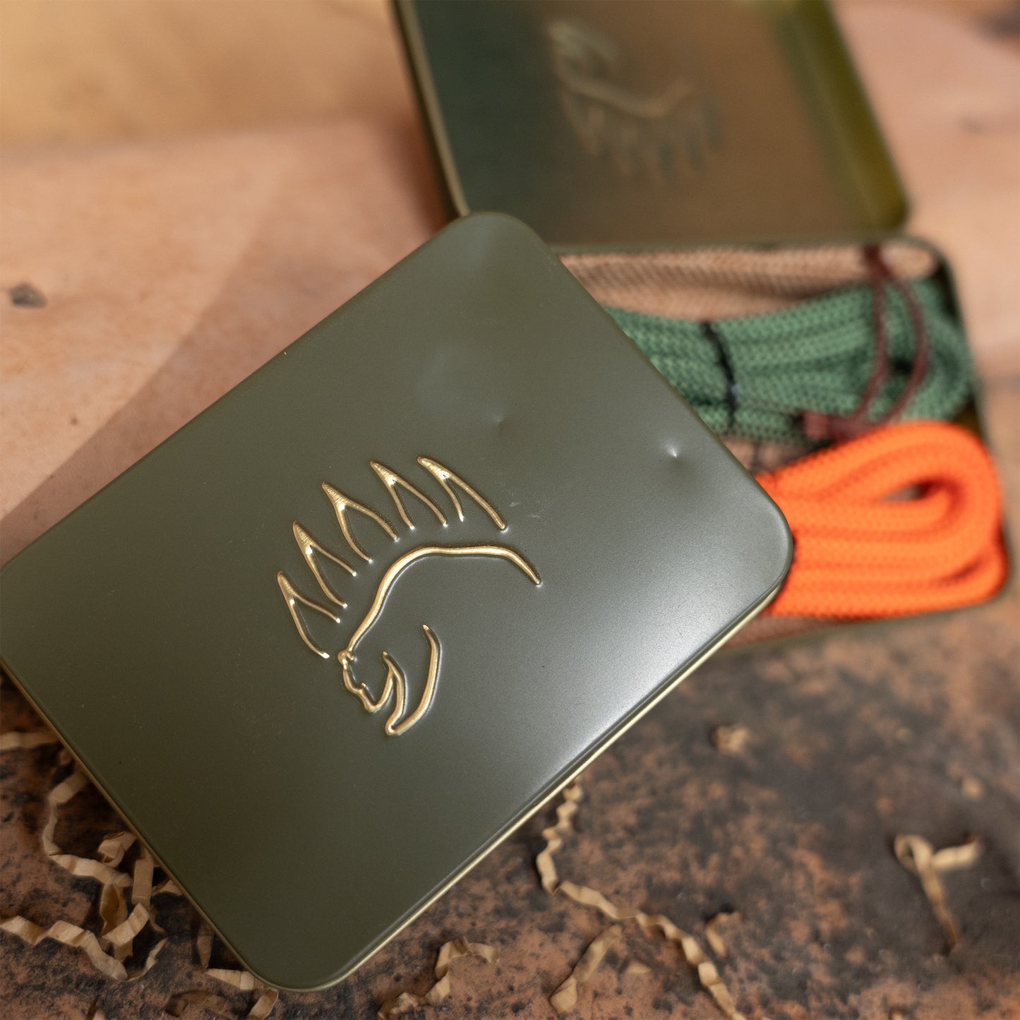 Outdoor camping knot kit in a green embossed tin with minor dents, featuring orange and green ropes for knot practice.