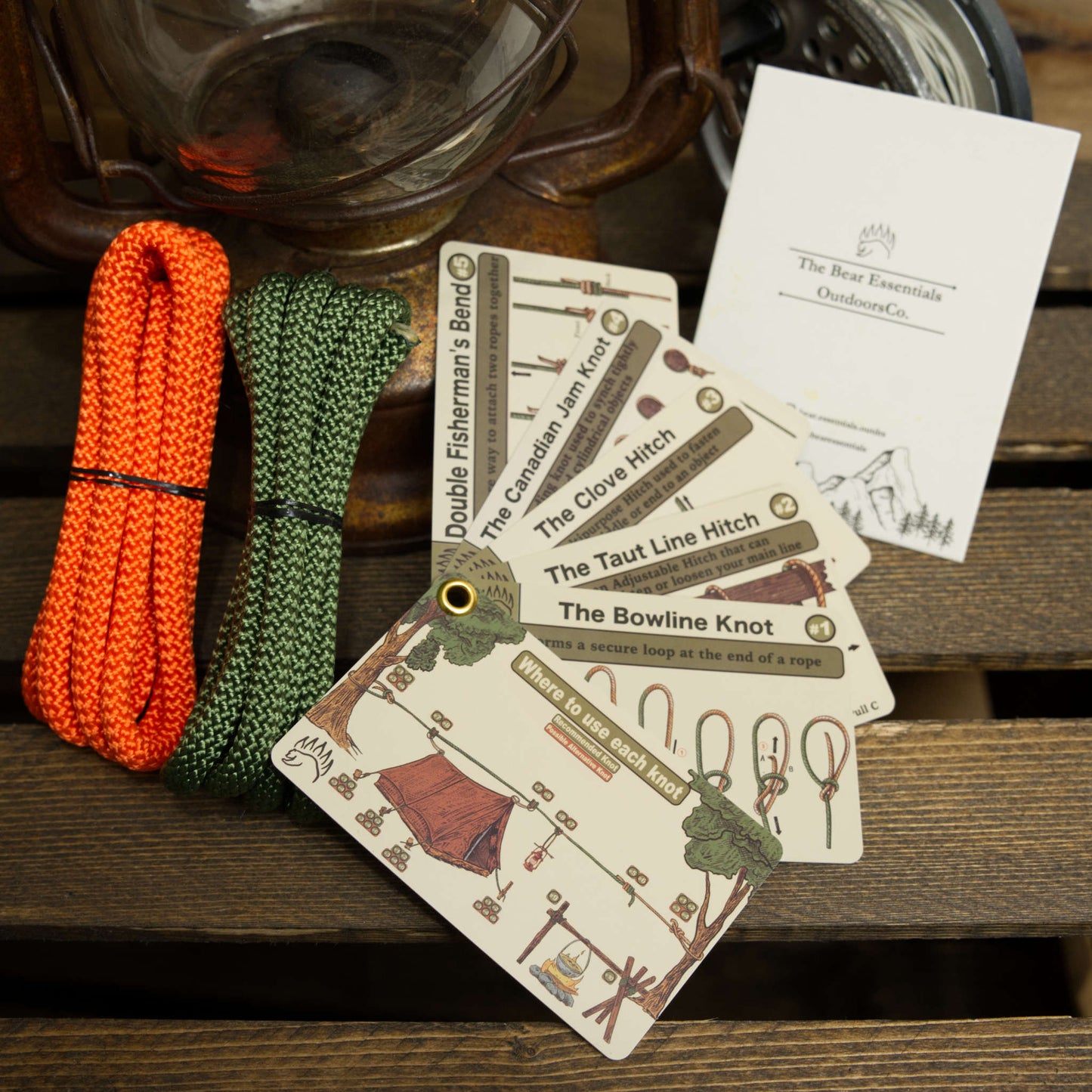 The Bear Essentials Knot Tying Kit with orange and green ropes, knot guide cards, and instruction sheet for mastering camping knots.