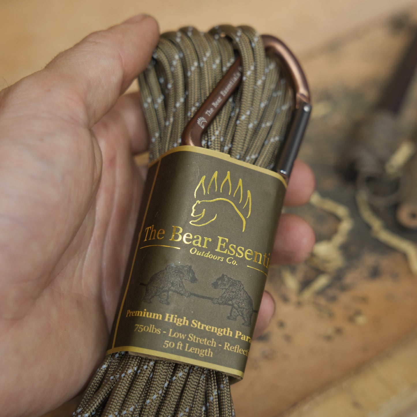 Hand holding Bear Essentials Premium Paracord with reflective camo sheath and carabiner, built for bushcraft and camping durability.