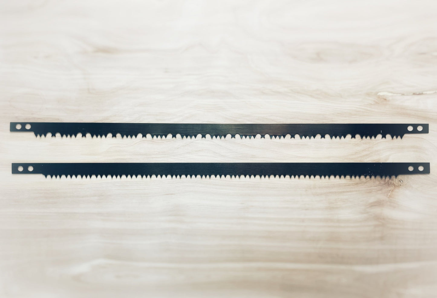 Two replacement saw blades from The Bucksaw Kit - Replacement Parts Bundle laid flat on a wooden surface, showcasing tooth design.