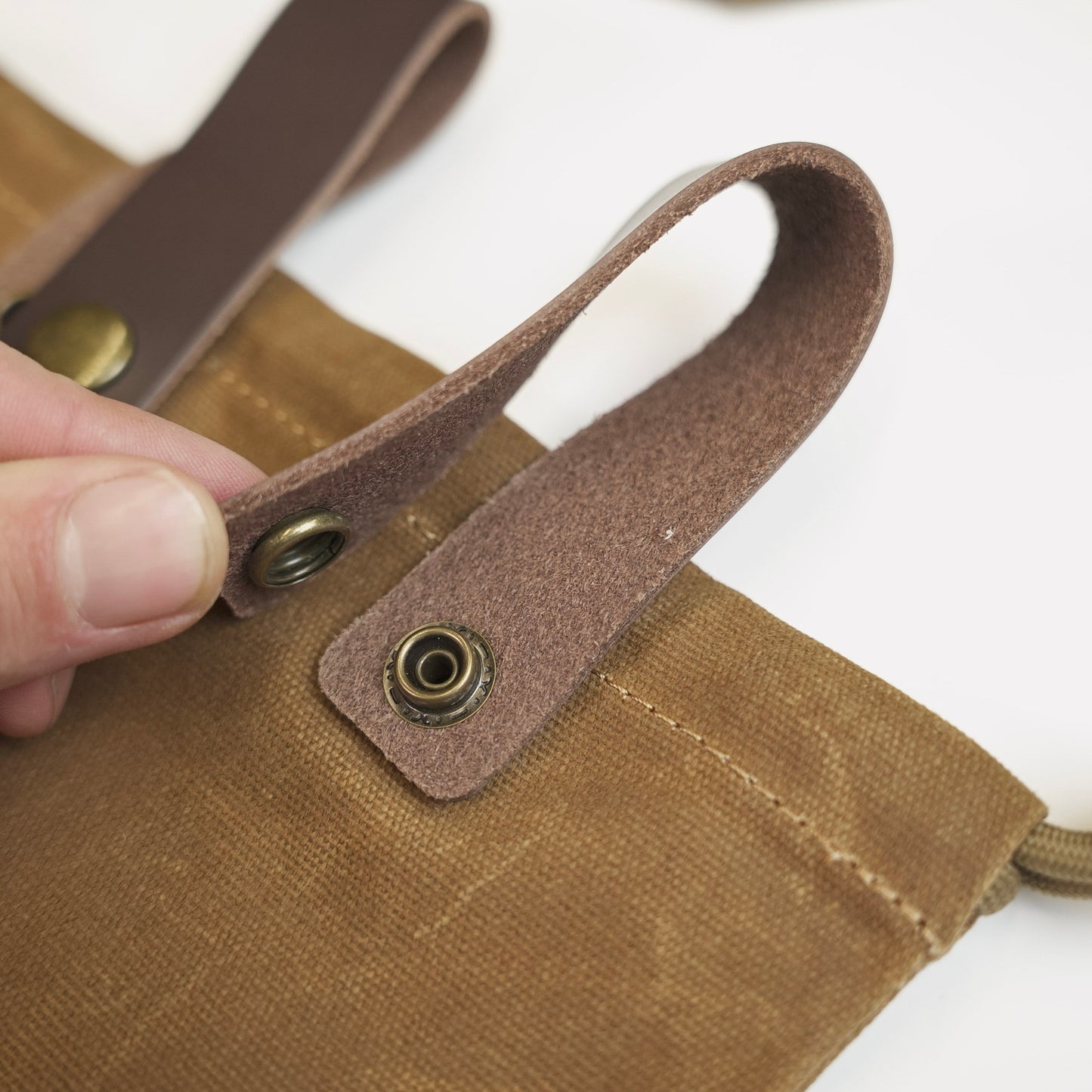 Close-up of the brass snap hardware and stitching on the waxed canvas axe holster.